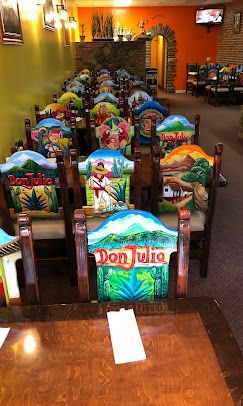 Colorful wooden chairs arranged in rows inside a warmly lit room, each with painted backrests.
