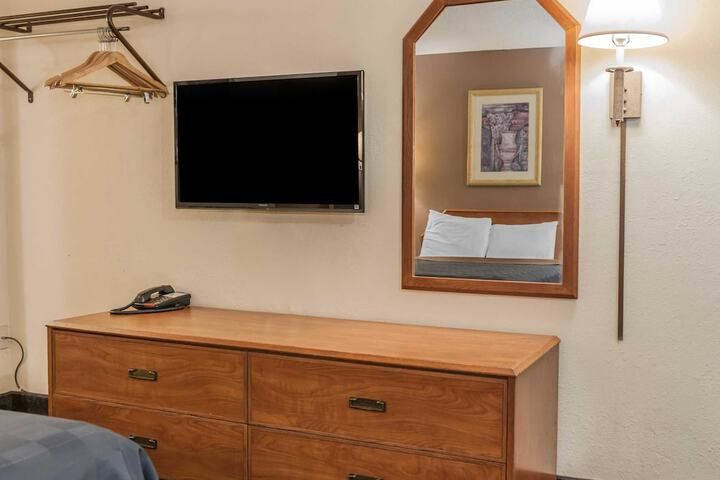 Hotel room wall with TV, dresser, mirror, lamp, and coat hangers