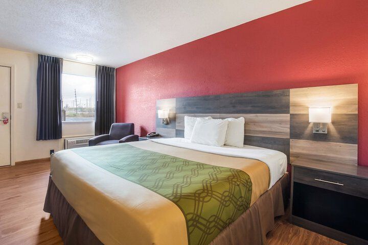 Hotel room with a bed, red accent wall, bedside lamps, and a window seat near the window