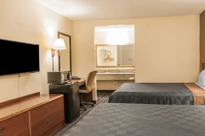 Motel room with two double beds, TV, desk, lamp, and wall mirror.