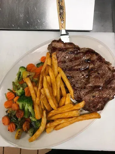 Steak with fries and mixed vegetables on a white plate with a fork at the top.
