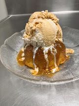 Ice cream sundae with caramel sauce on a clear glass plate on a stainless steel counter.