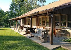 Wooden cabin porch with benches and tables beside a green lawn