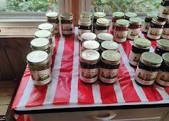Jars of homemade preserves and sauces arranged on a red-and-white striped cloth by a window