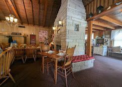 Rustic dining room with wooden tables, chairs, stone fireplace, and log beam ceiling