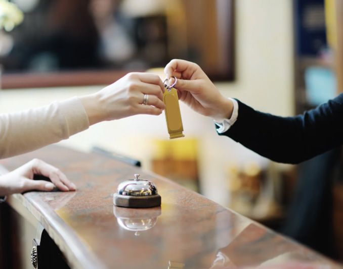 Hotel employee handing room key to a guest over a reception desk.