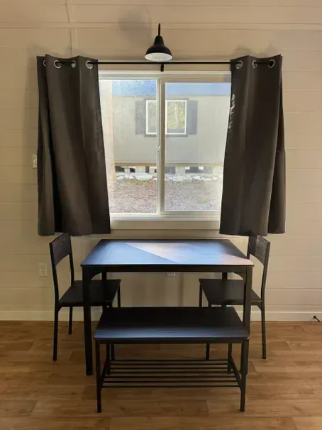 A dining set with two chairs and a bench sits centered in front of a window with dark curtains and an overhead light.