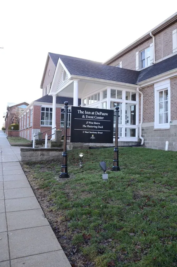 A sign for The Donald D. Paoli & Sons Funeral Home stands on a lawn in front of a brick building with white trim.
