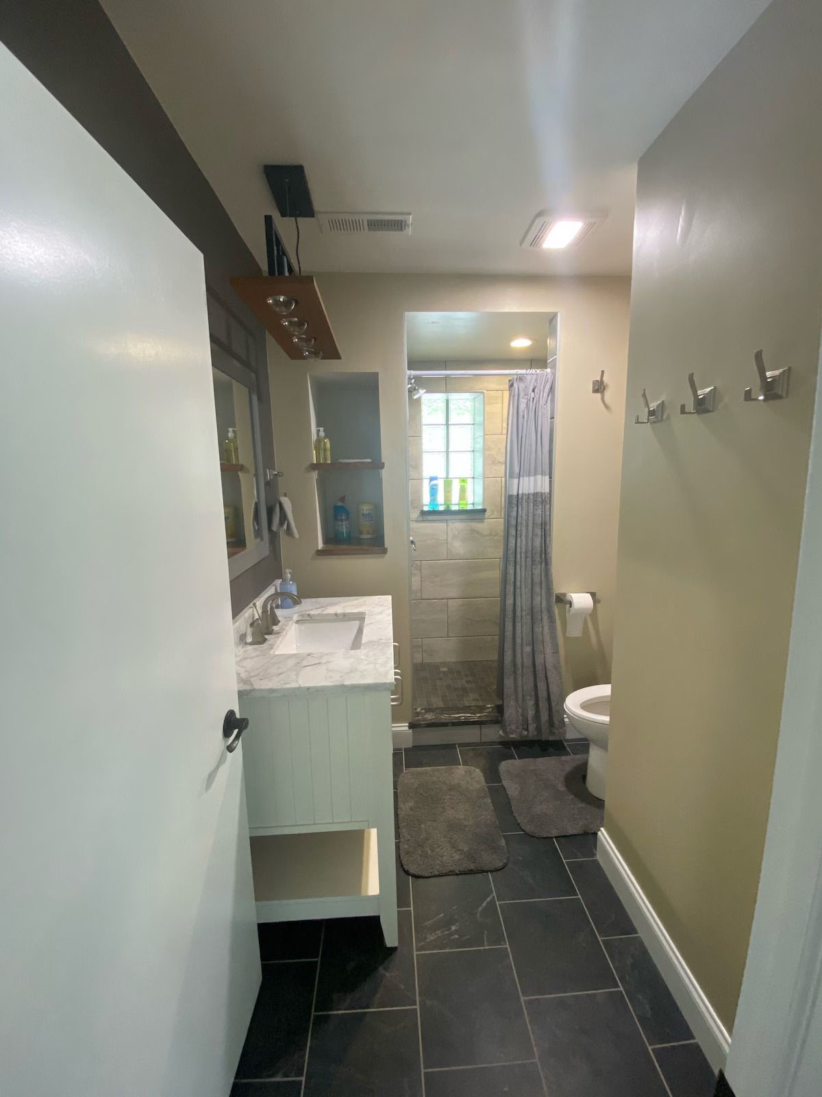 A bathroom with a white vanity, a tiled floor, and a shower area with a grey curtain, viewed from the doorway.