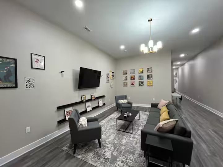 A modern living room with a grey sofa, matching armchair, a wall-mounted TV above a shelf, and art hung on light walls.