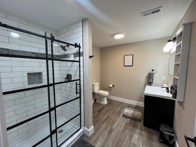 Modern bathroom with a glass-enclosed shower, wood-look flooring, a toilet, and a vanity with a white countertop.