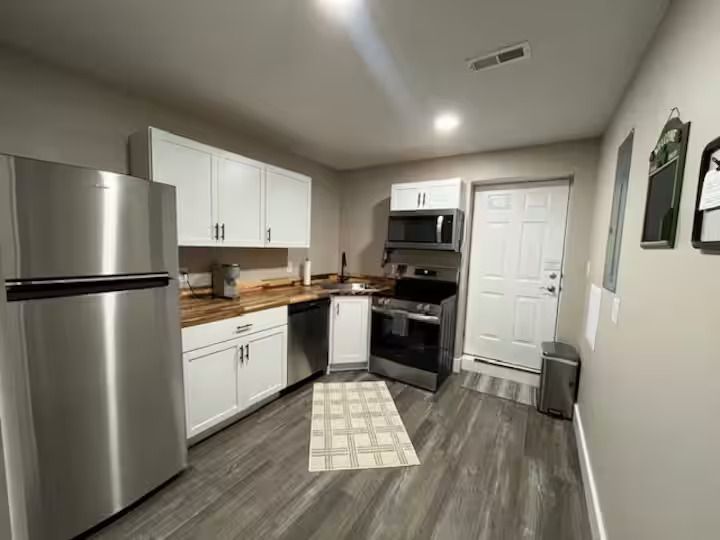 A kitchen with white cabinets, wood-look countertops, stainless steel appliances, and gray flooring.