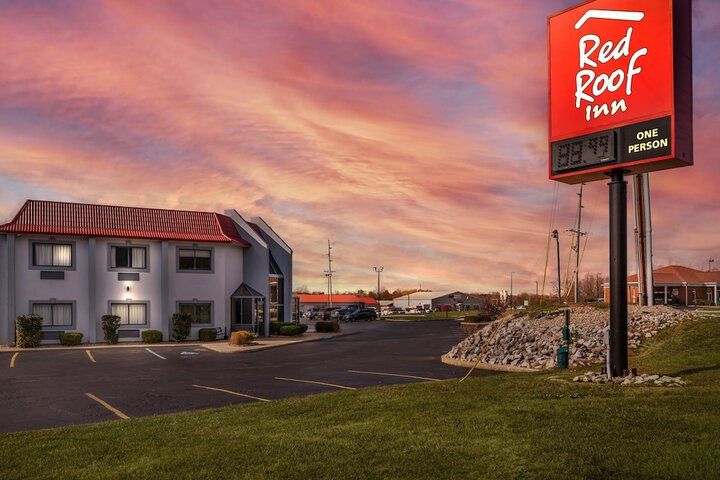Red Roof Inn motel at dusk with a bright red sign and empty parking lot under a colorful sky