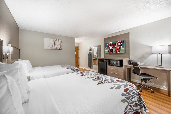 Hotel room with two beds, wall-mounted TV, desk, lamp, and hardwood floor