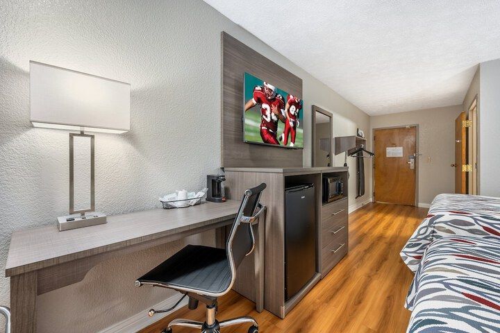 Hotel room with desk, chair, TV, mini fridge, bed, and hallway view