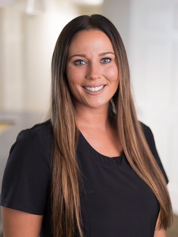 Dental hygienist with long hair wearing black scrubs smiling at the camera