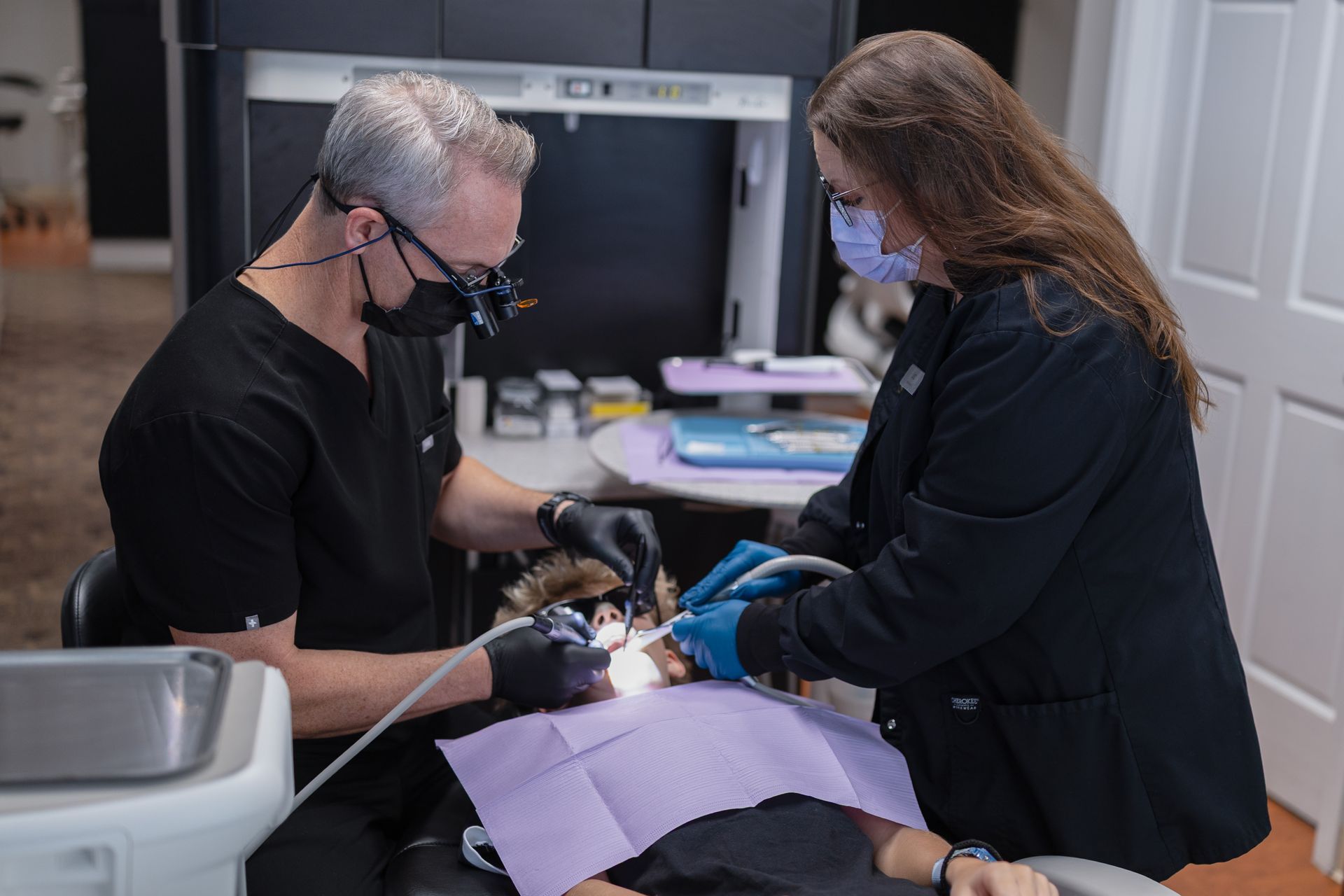 Male dentist working on middle aged male patient lying in chair