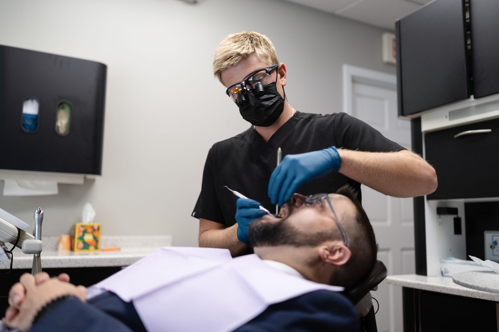 Middle aged man lying back in the dental chair with a dentist inspecting teeth