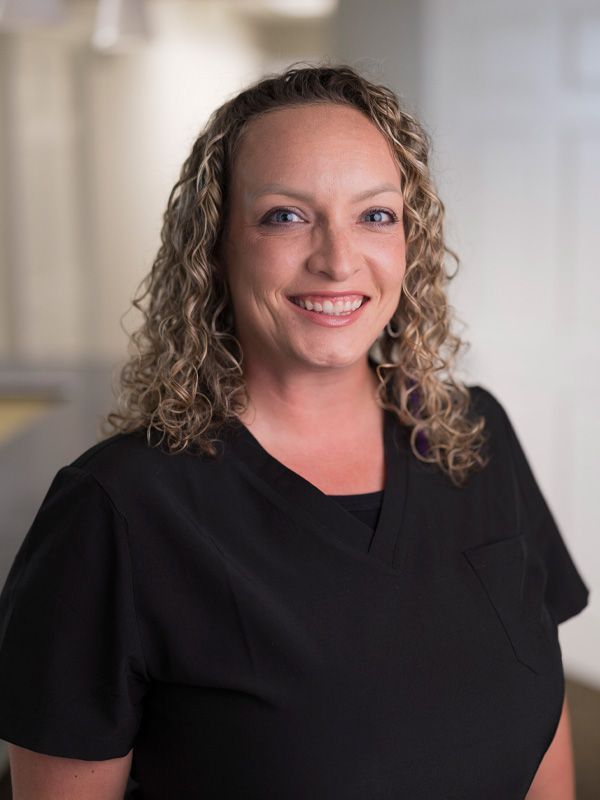 Woman with curly hair wearing black smiling at camera in a dentist office