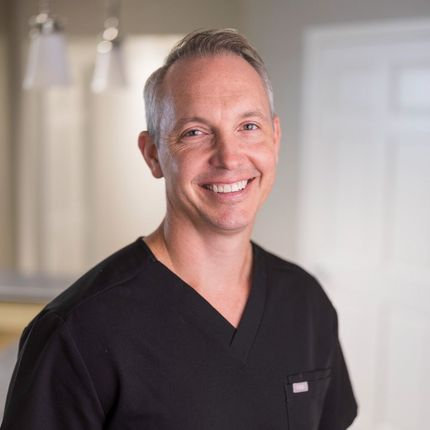 A dentist in a black shirt is smiling for the camera