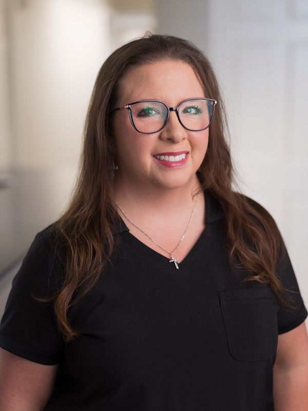 Woman with glasses in scrubs smiling at camera