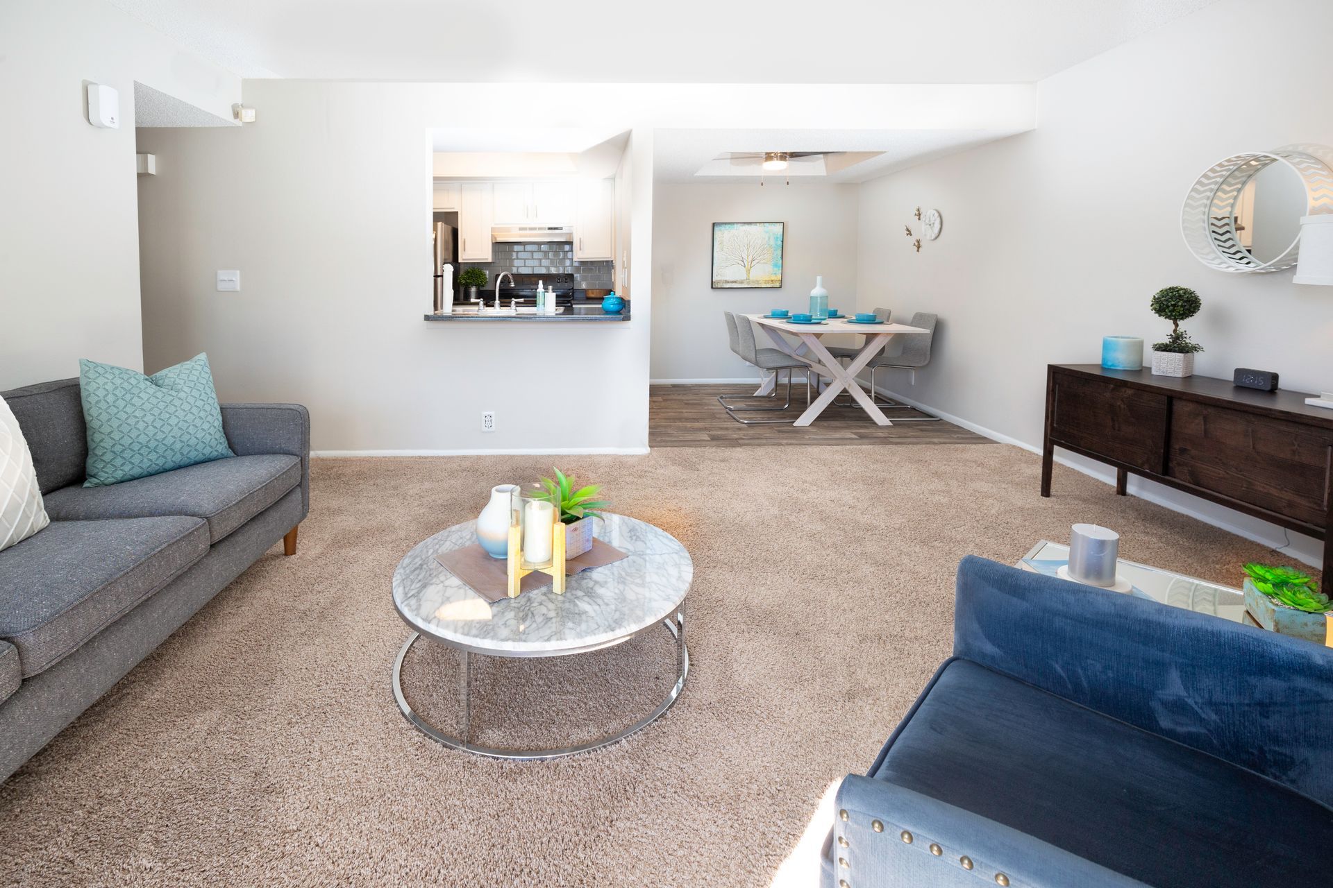 a living room with a couch , chair , coffee table and dining room in the background .