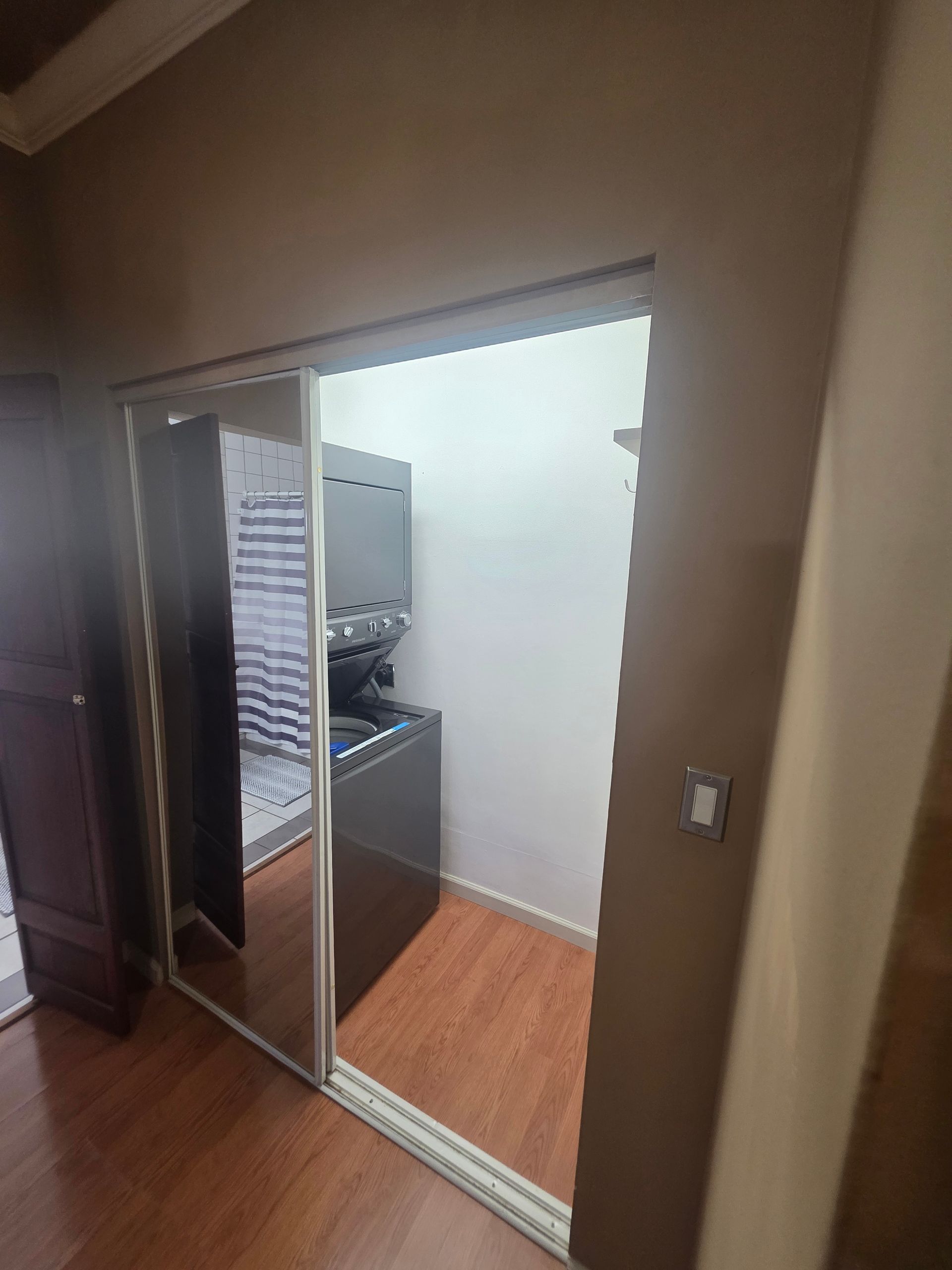 A laundry room with mirrored sliding doors, stacked washer and dryer, and wood floors.