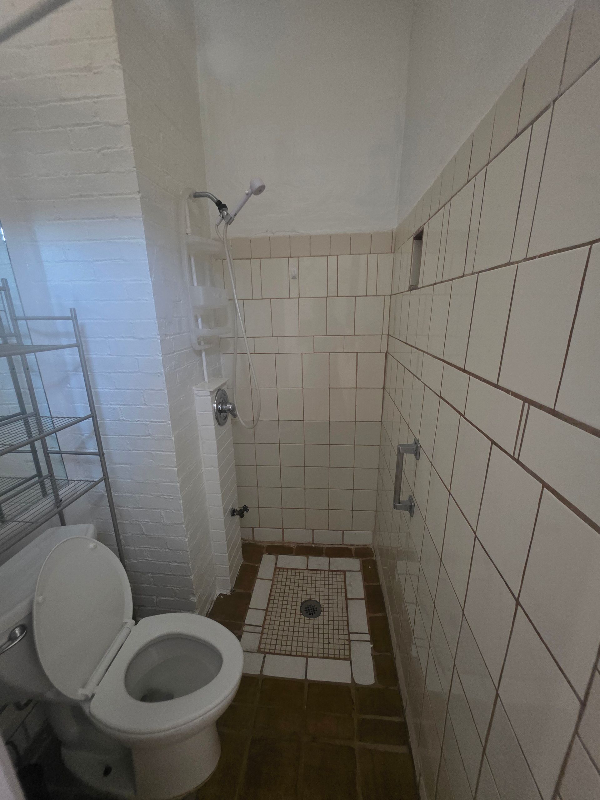 Small bathroom with a toilet, shower, and tiled walls.