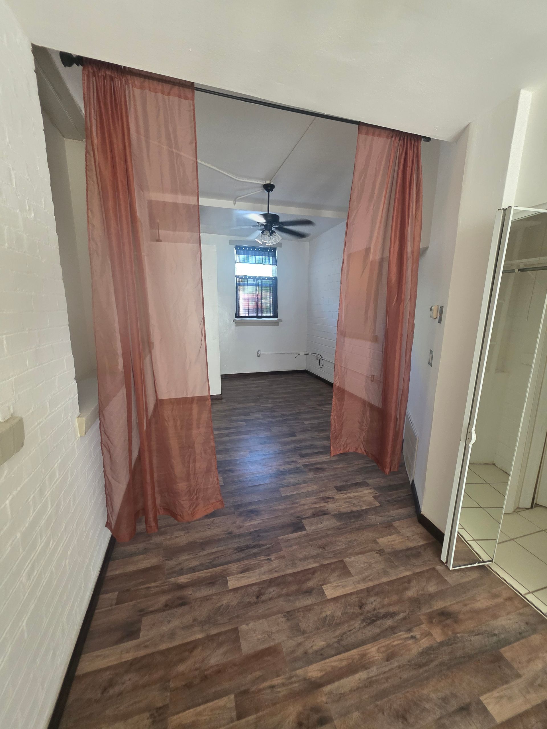 Narrow doorway with sheer orange curtains, leading to a room with a ceiling fan and window.