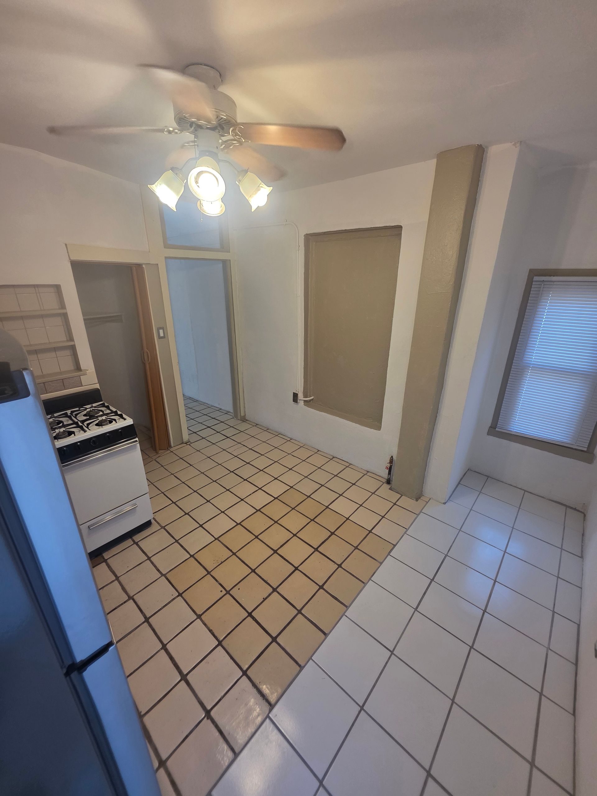 Kitchen with white tile floor, stove, and refrigerator. A door leads to another room.