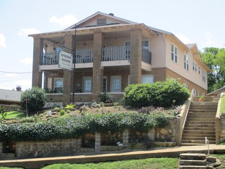 Two-story beige and stone building with a balcony, stairs, and a sign that reads, 