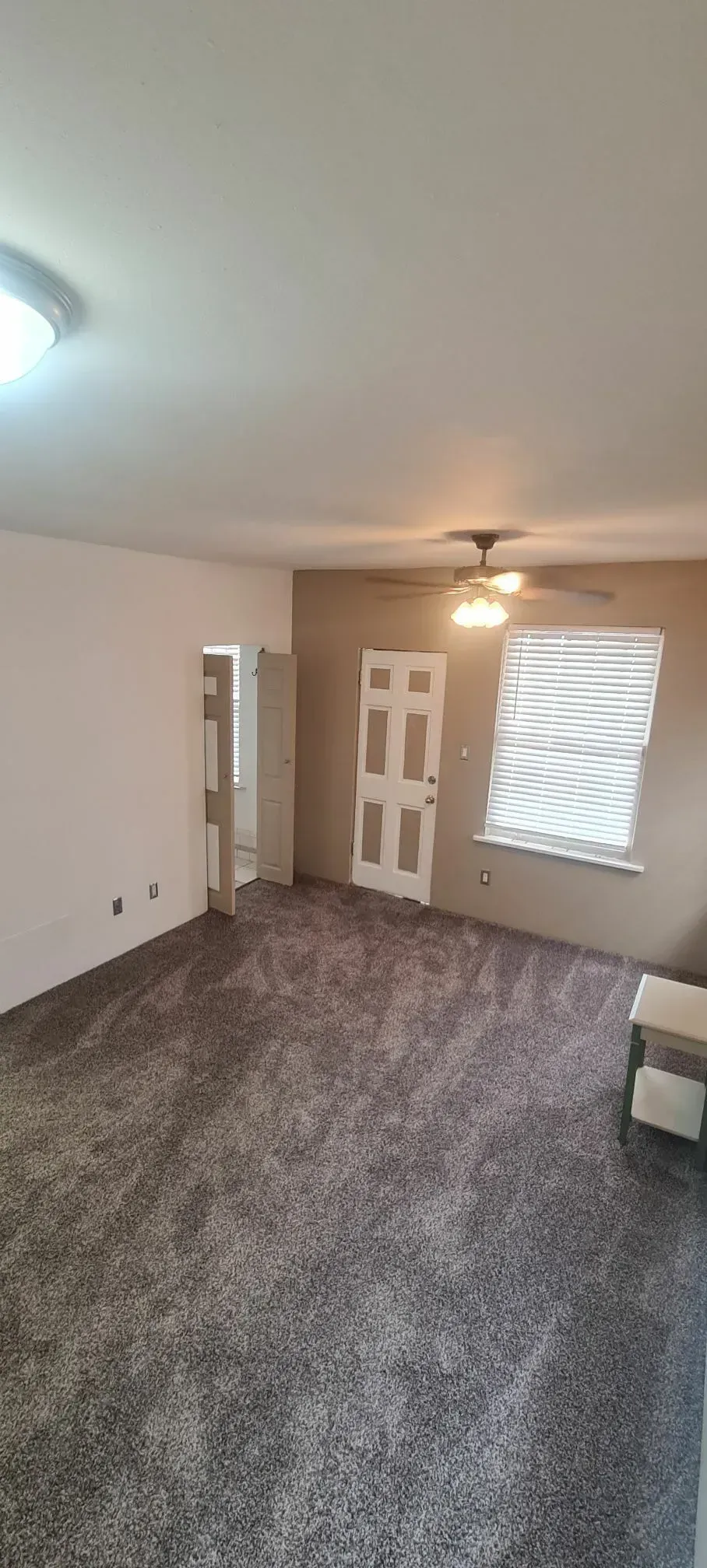 An empty living room with a ceiling fan and a door.