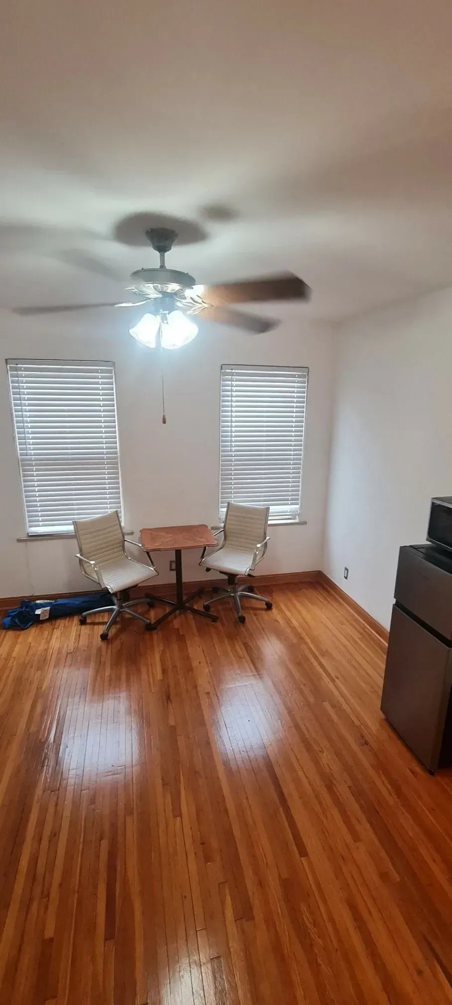 A living room with hardwood floors , two chairs , a table and a ceiling fan.