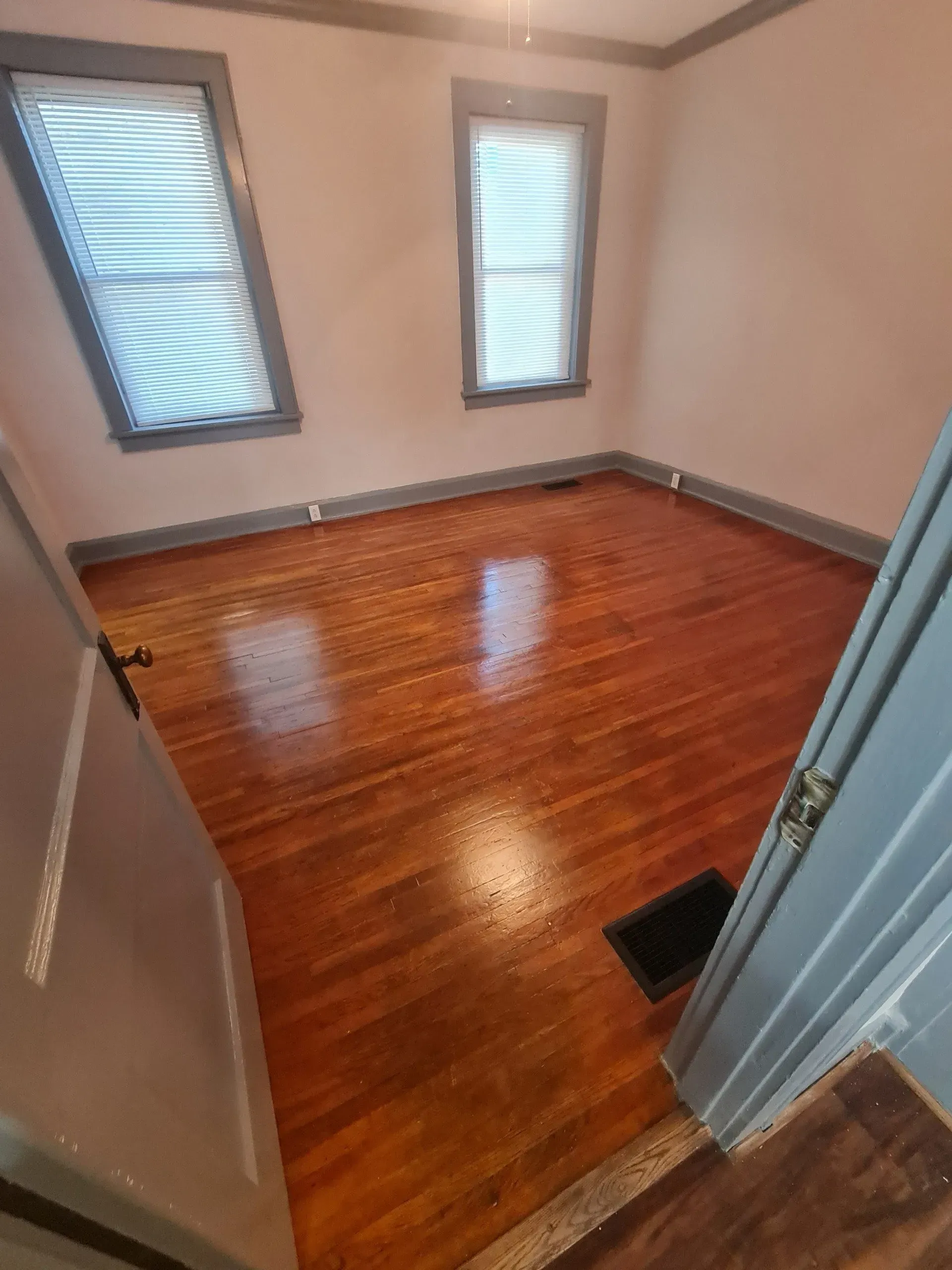 An empty room with hardwood floors and two windows.