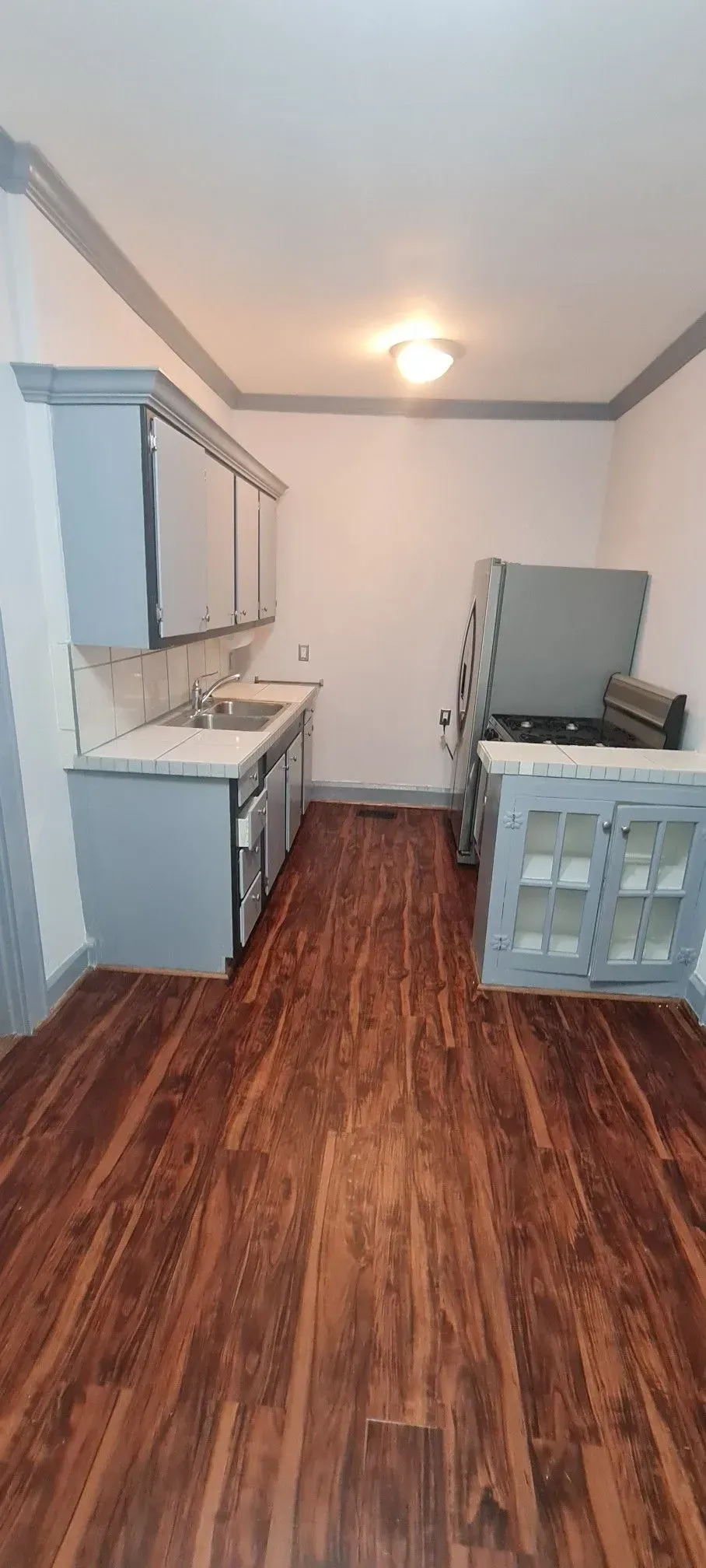 A kitchen with hardwood floors , a sink , a refrigerator , and a stove.