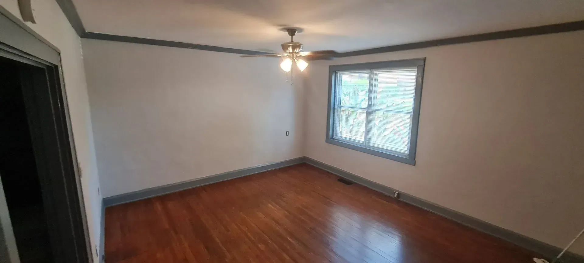 An empty living room with hardwood floors and a ceiling fan.