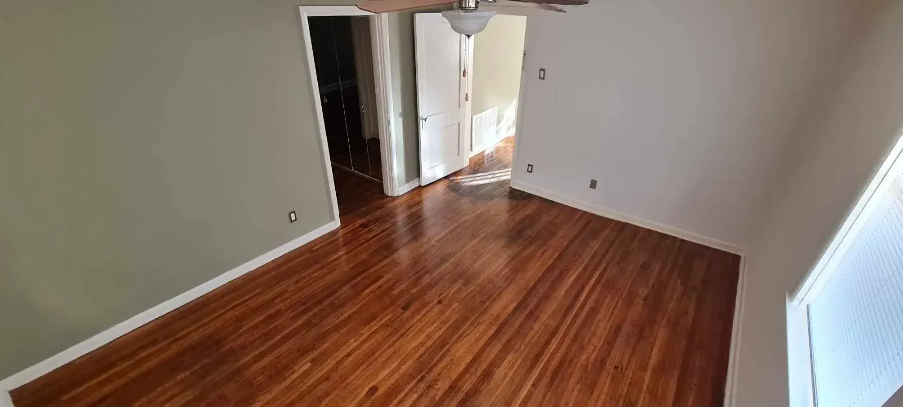 An empty room with hardwood floors and a ceiling fan.