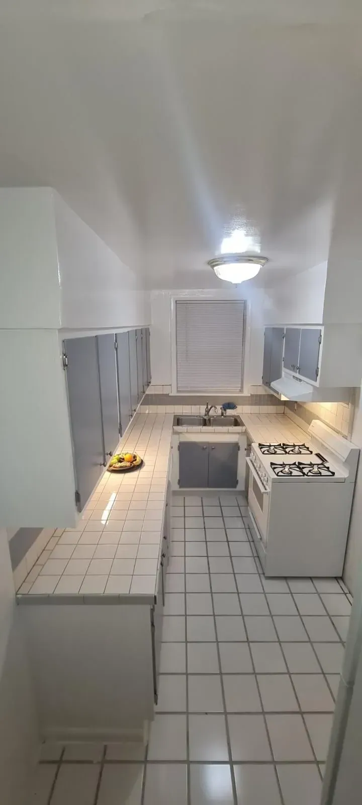 A kitchen with white cabinets , tile floors , a stove and a sink.