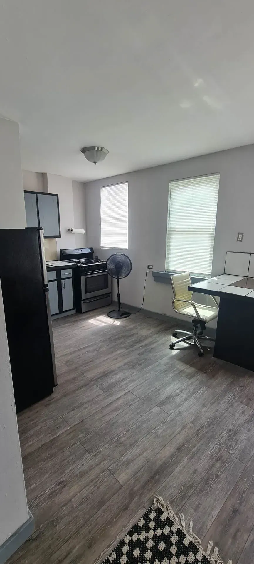 A living room with a stove , refrigerator , desk and chair.