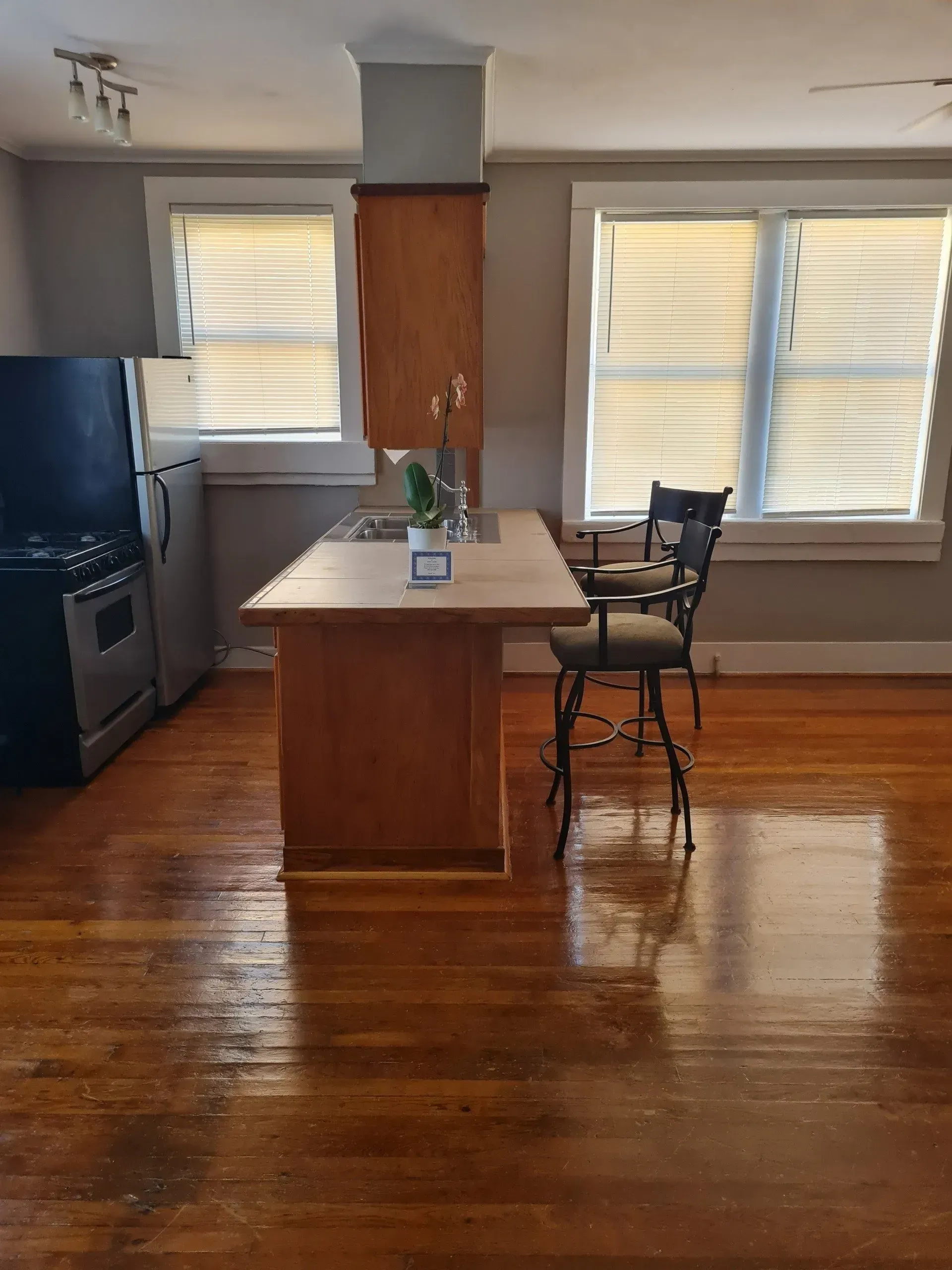 A kitchen with a large island , stools , a stove , and a refrigerator.