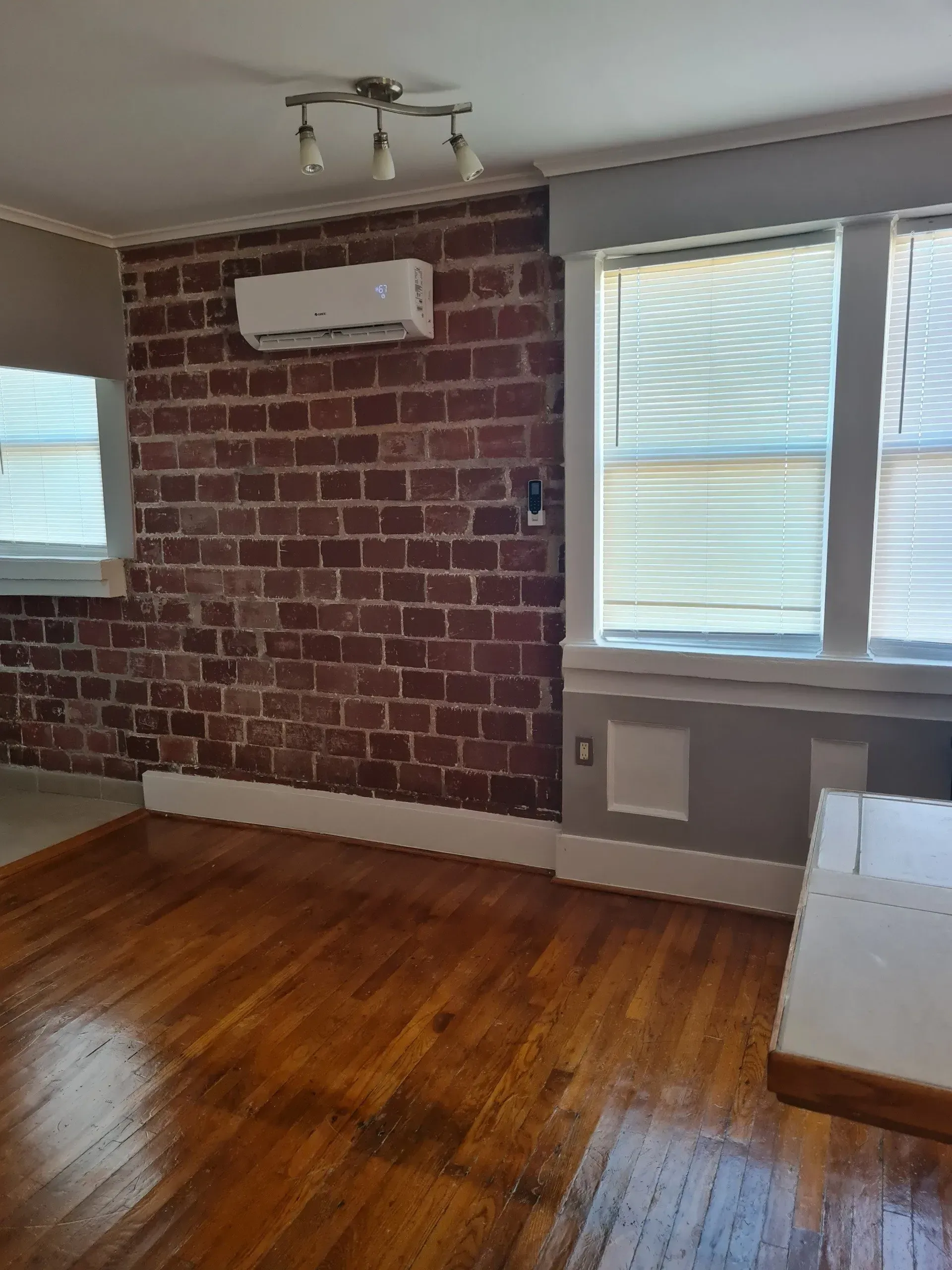 A living room with hardwood floors , a brick wall , and a window.