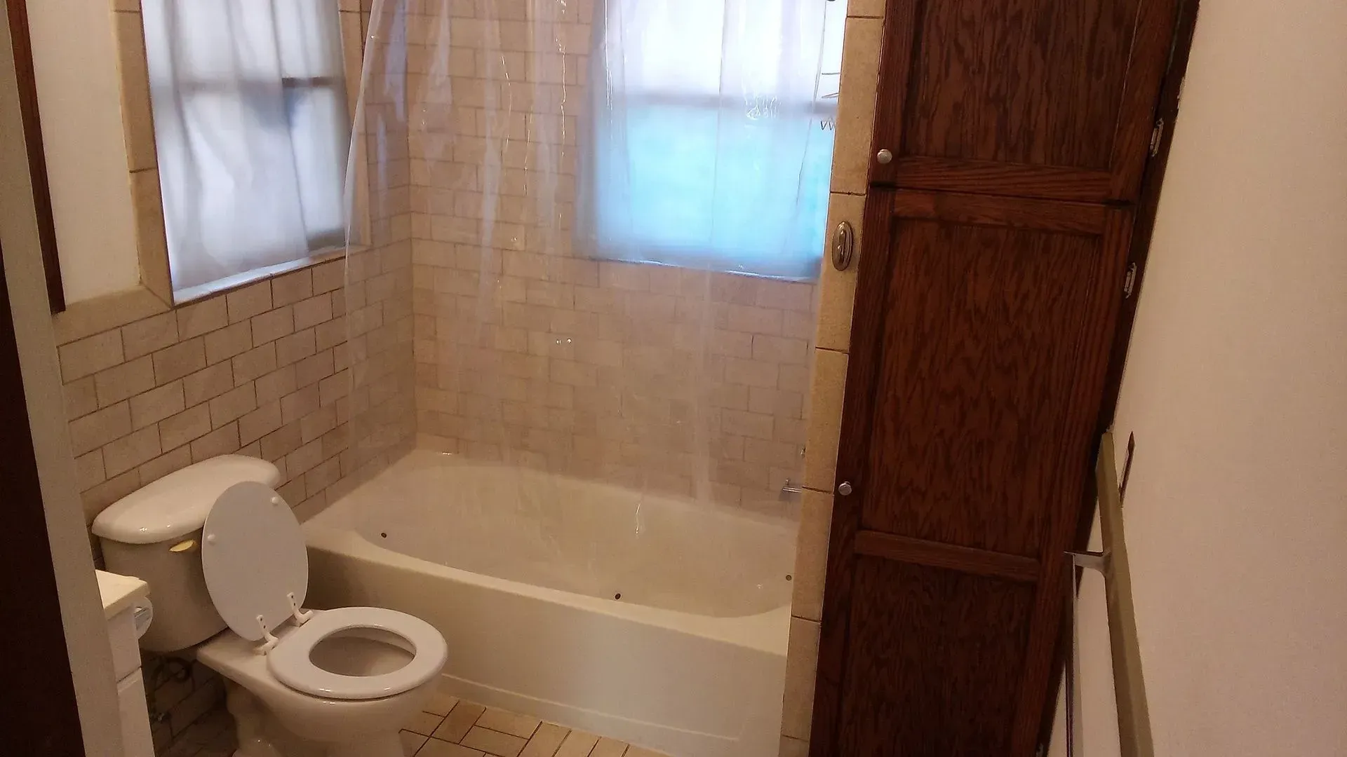 A bathroom with a toilet , bathtub and window.