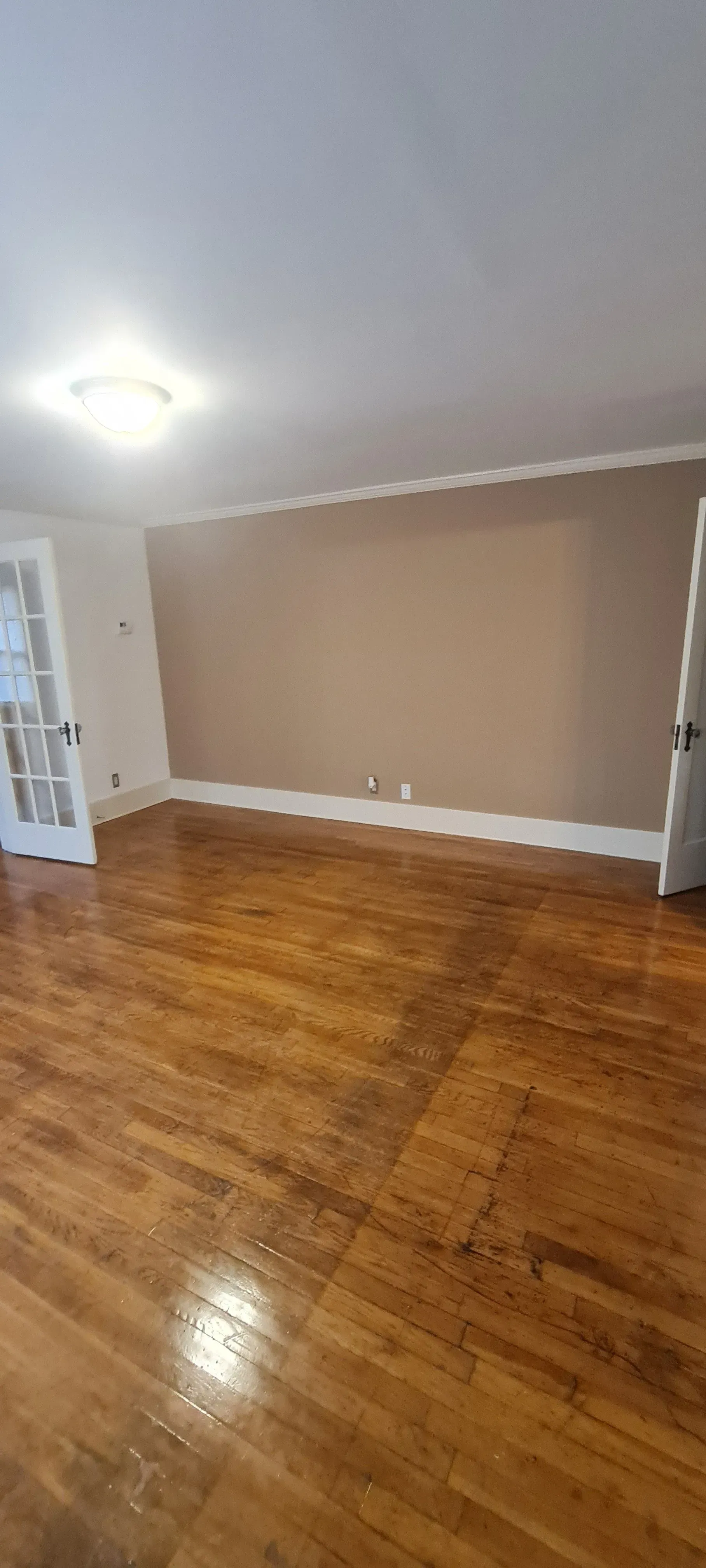 An empty living room with hardwood floors and beige walls.