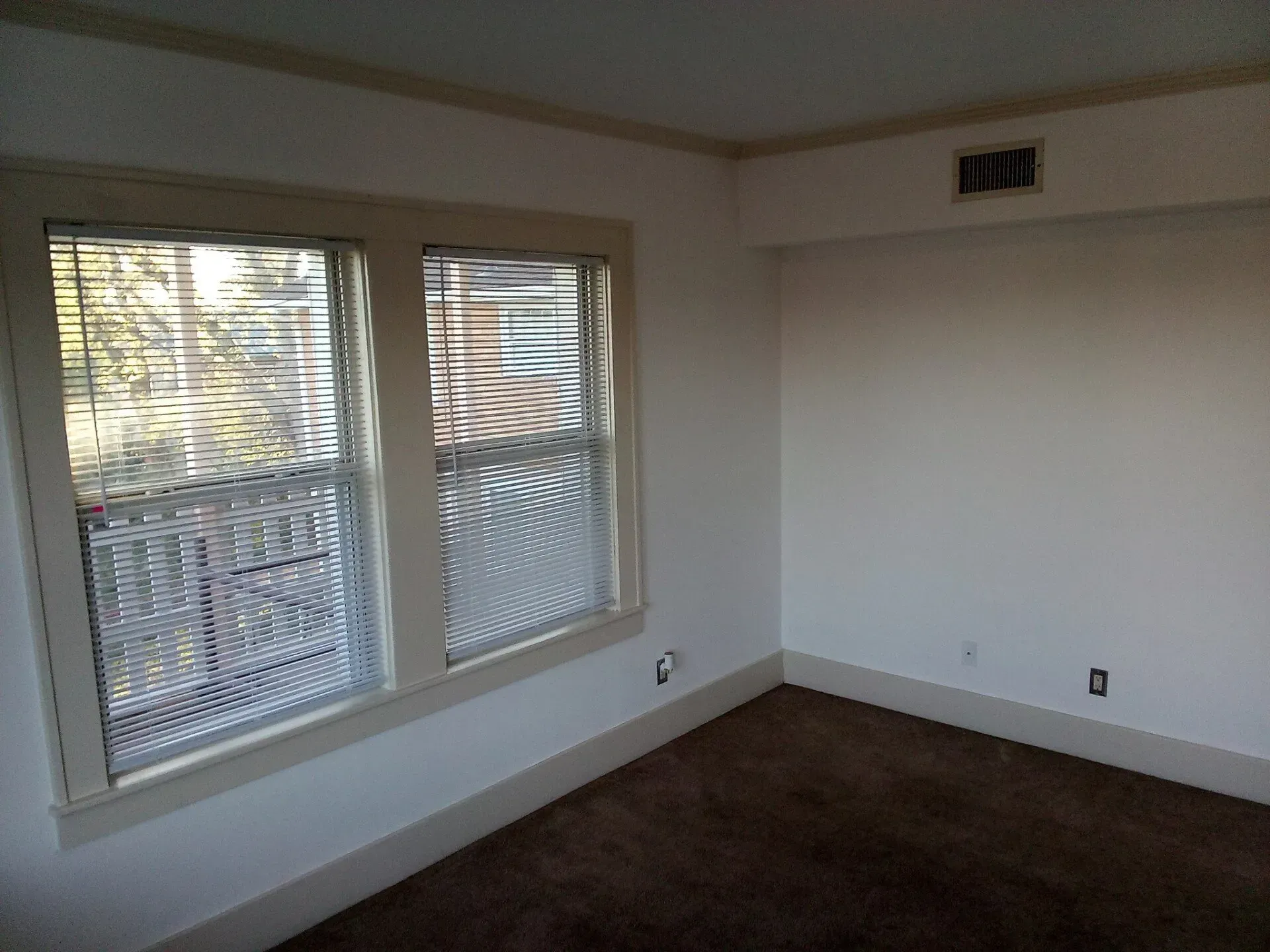 An empty room with two windows and blinds on them