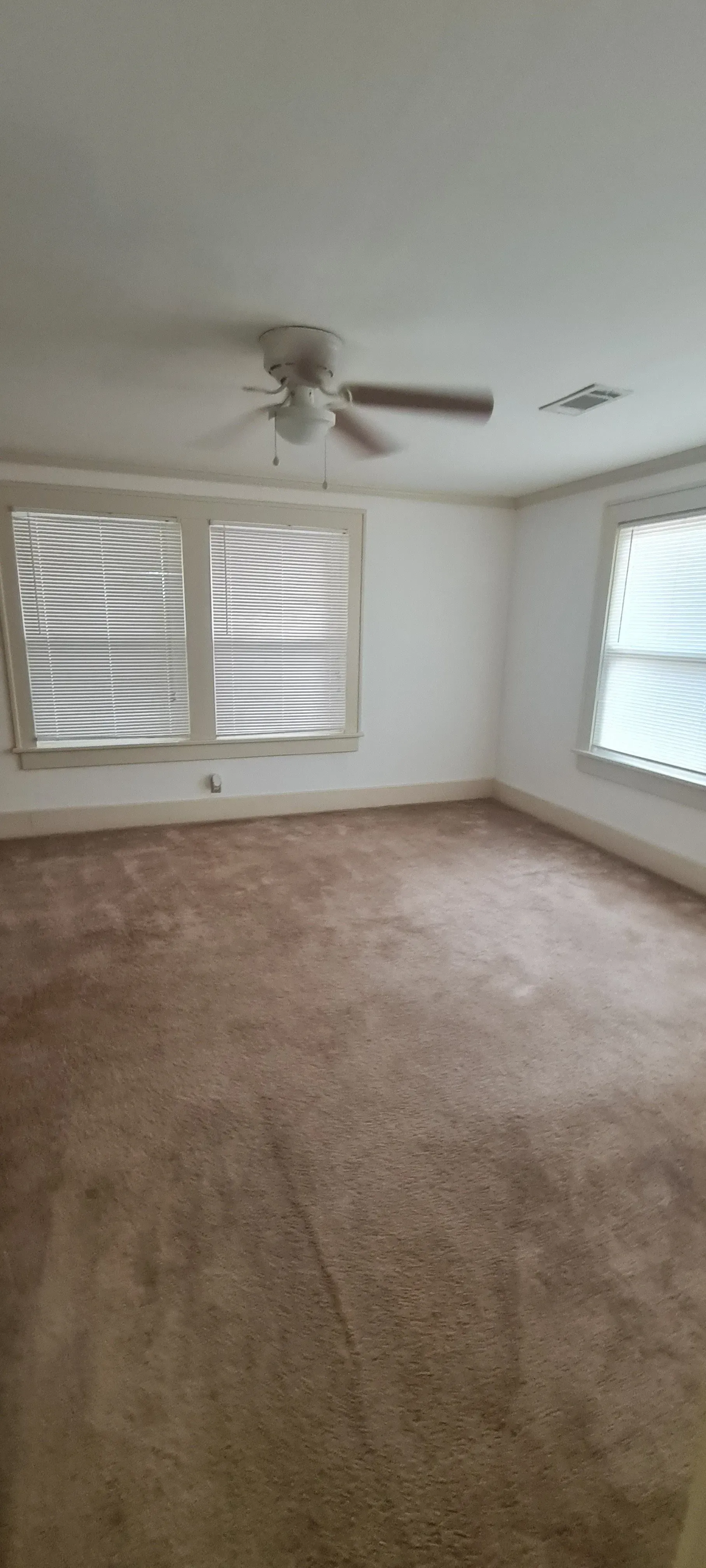 An empty living room with a ceiling fan and two windows.