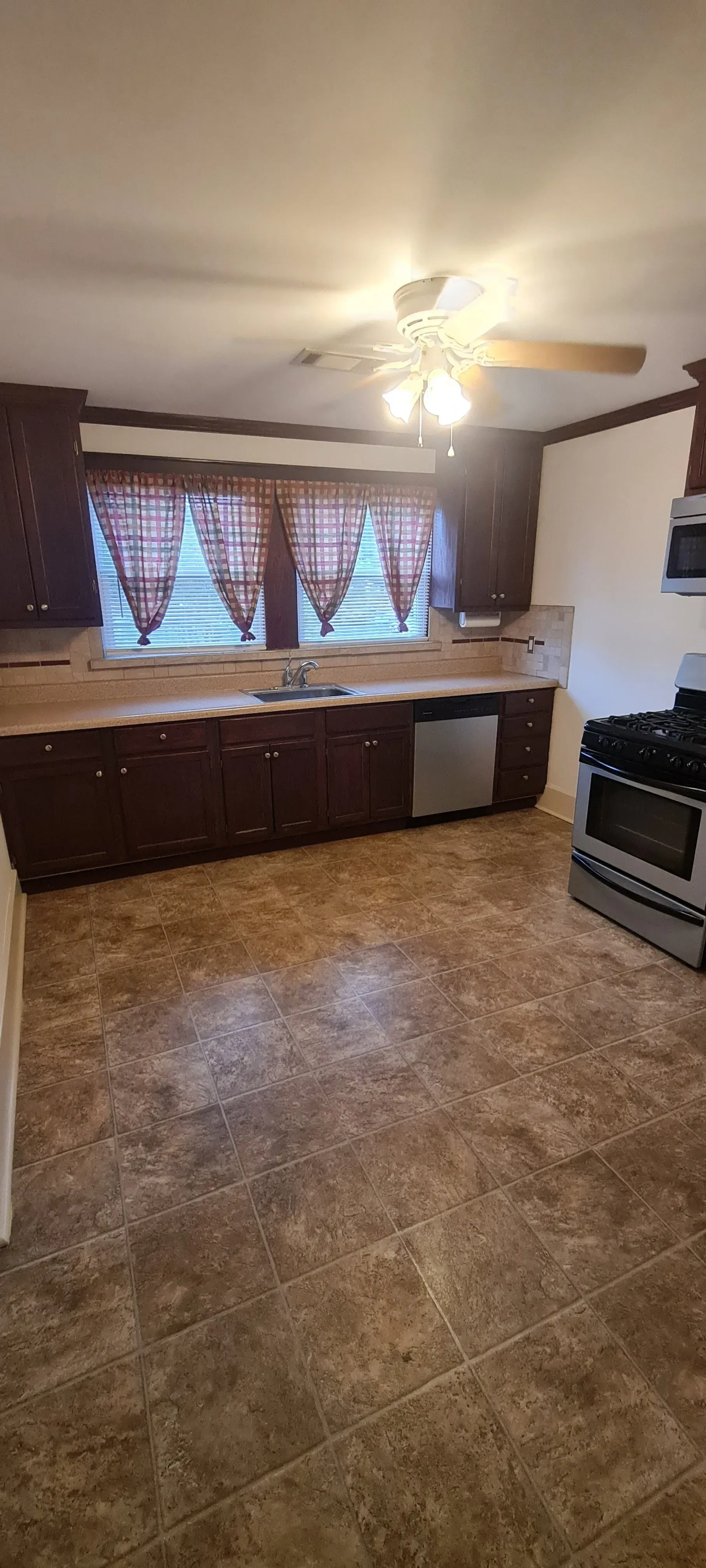 A kitchen with a stove , sink , dishwasher and ceiling fan.
