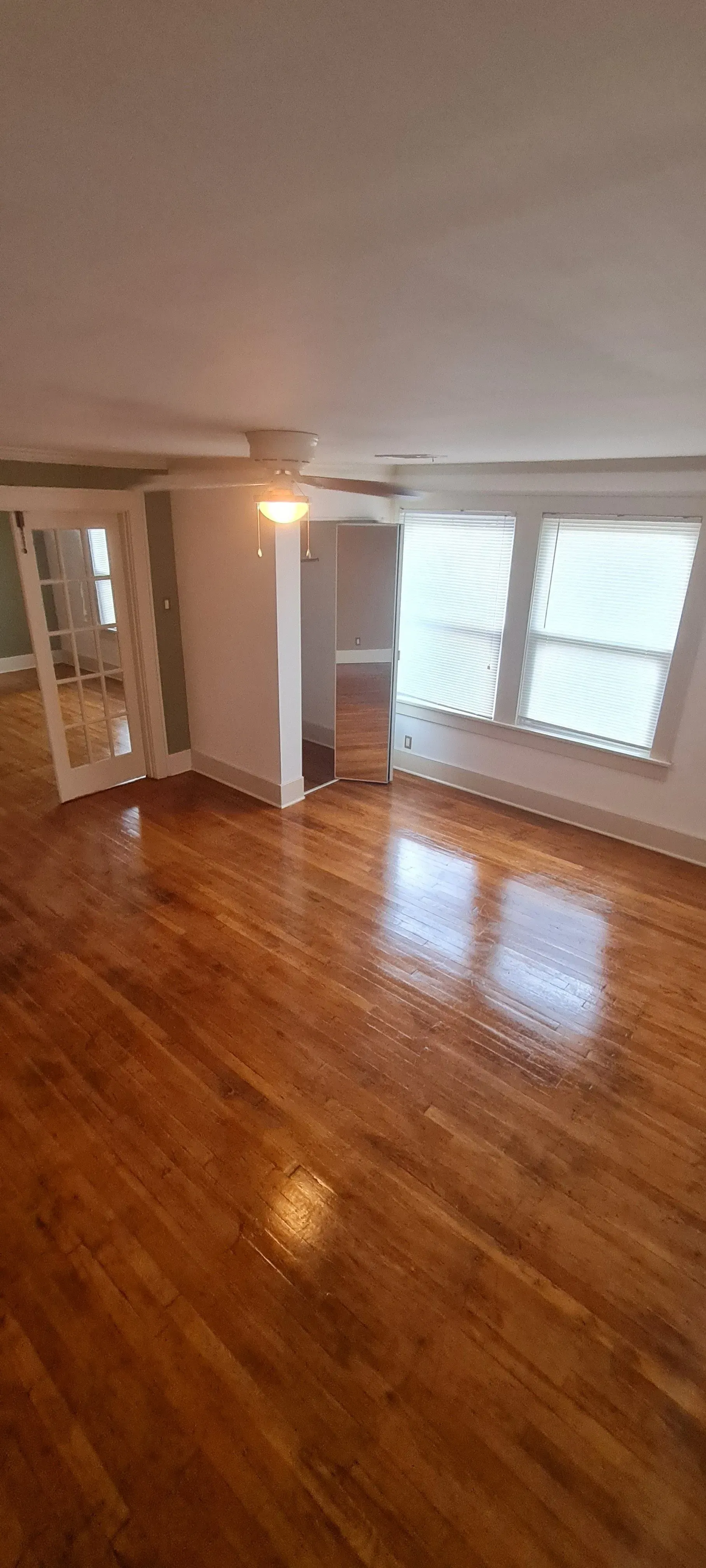 An empty living room with hardwood floors and two windows.