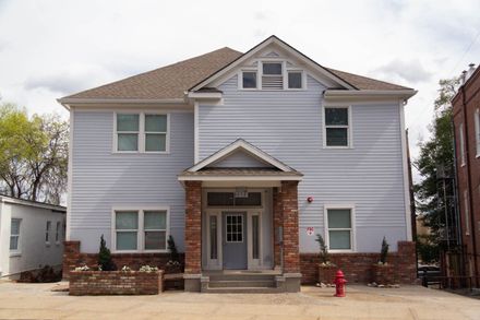 Light blue two-story building with brick accents and a gabled roof. A red fire hydrant sits in front.