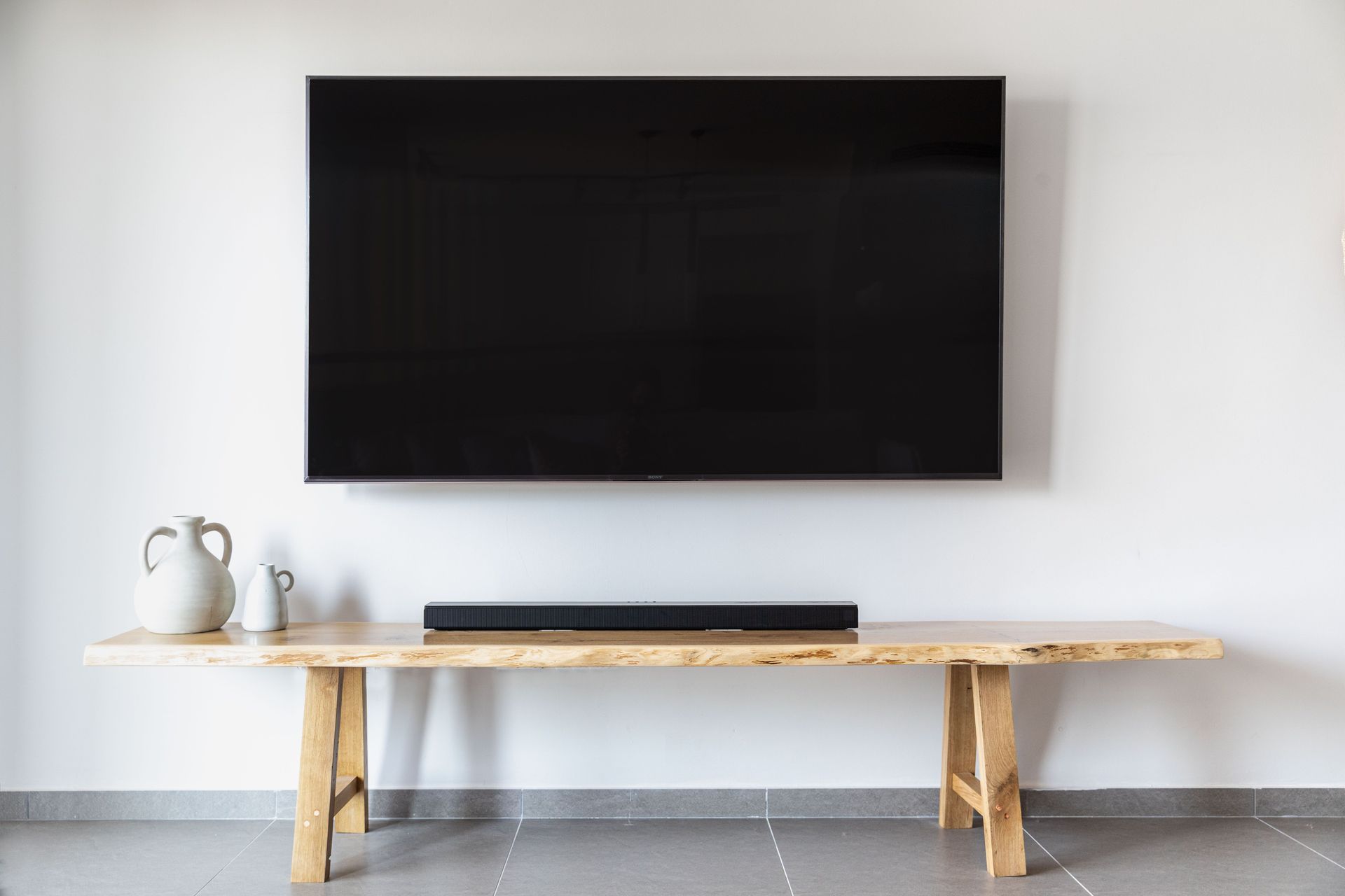 Minimalist living room with wall-mounted TV above a wooden bench and a small kettle on the left