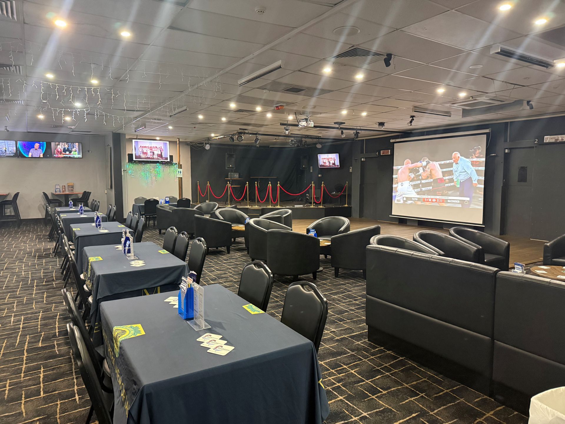 Conference room with rows of black chairs and tables facing a large stage and projection screens — Tennant Creek Memorial Club & Steak House in Tennant Creek, NT